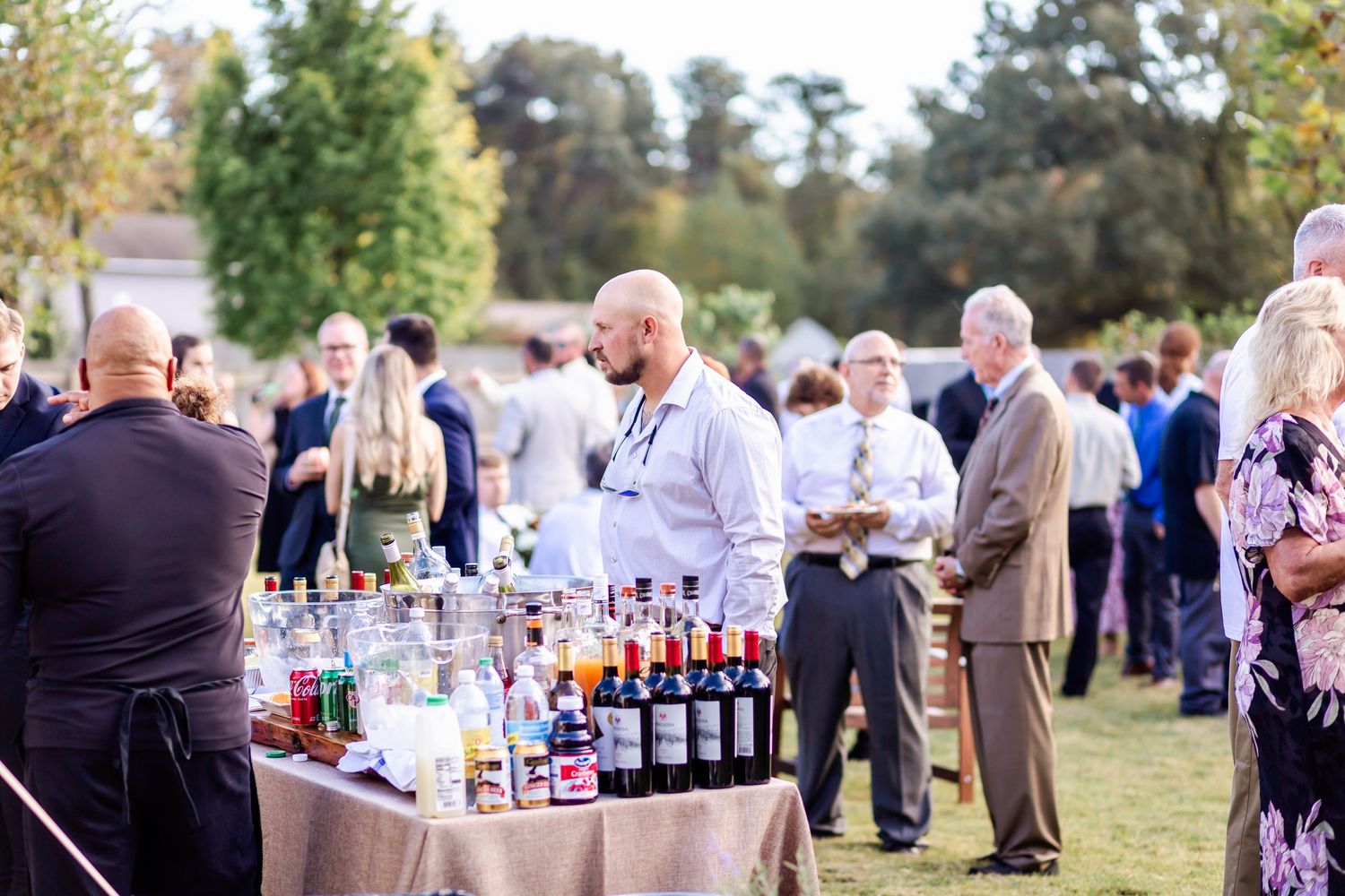 Outdoor wedding reception with guests mingling around cocktail tables and bar setups.