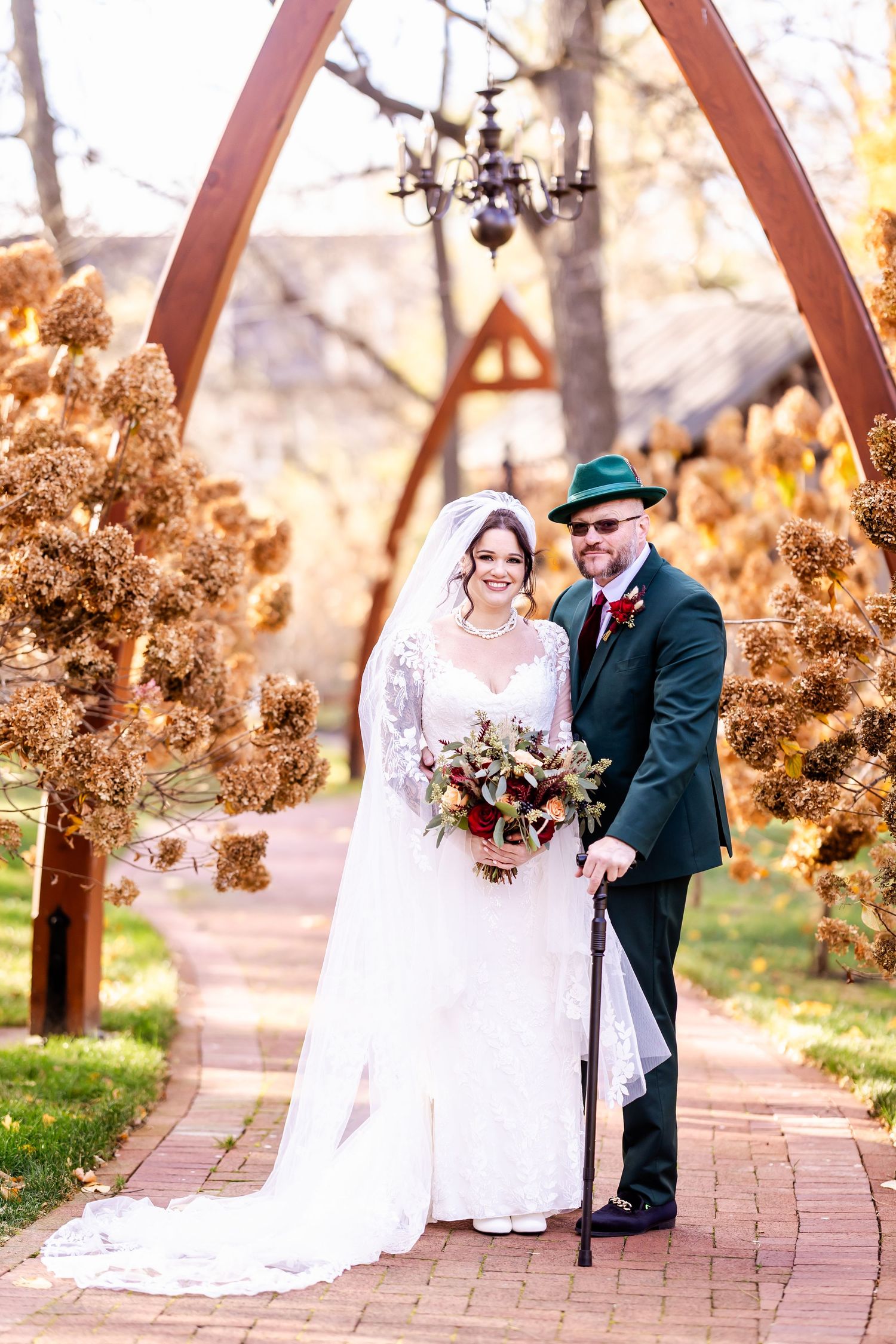 A wedding couple poses under rustic wooden arches surrounded by autumn foliage.
