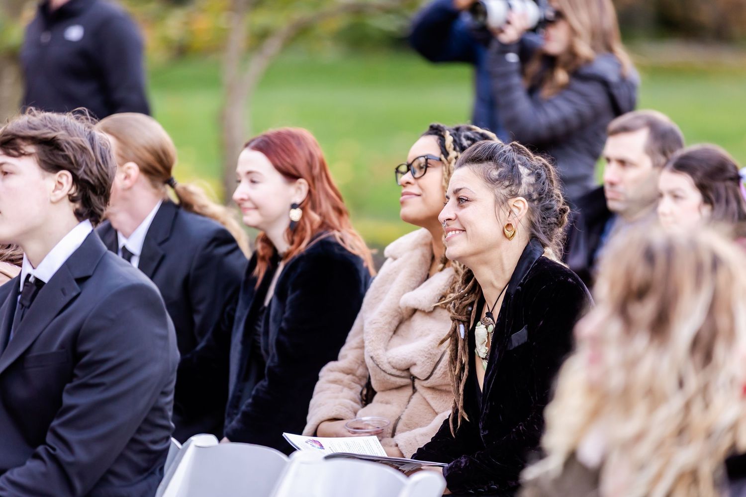 Wedding guests seated in rows during an outdoor ceremony with natural fall backdrop.