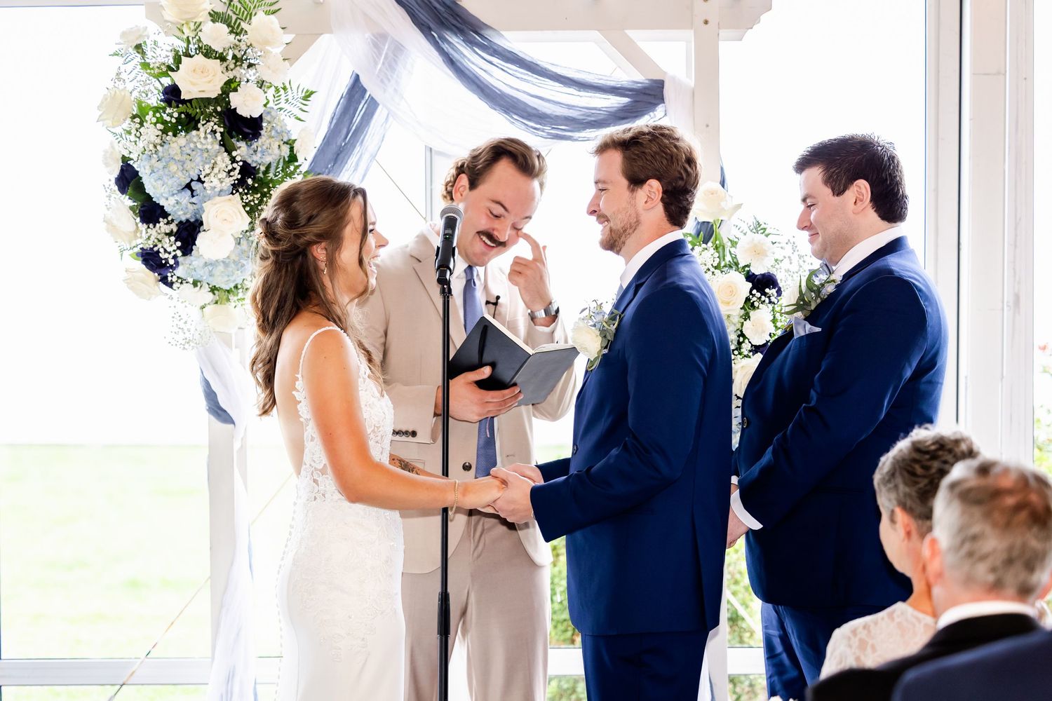Wedding ceremony proceedings in a light-filled room with floral decorations.