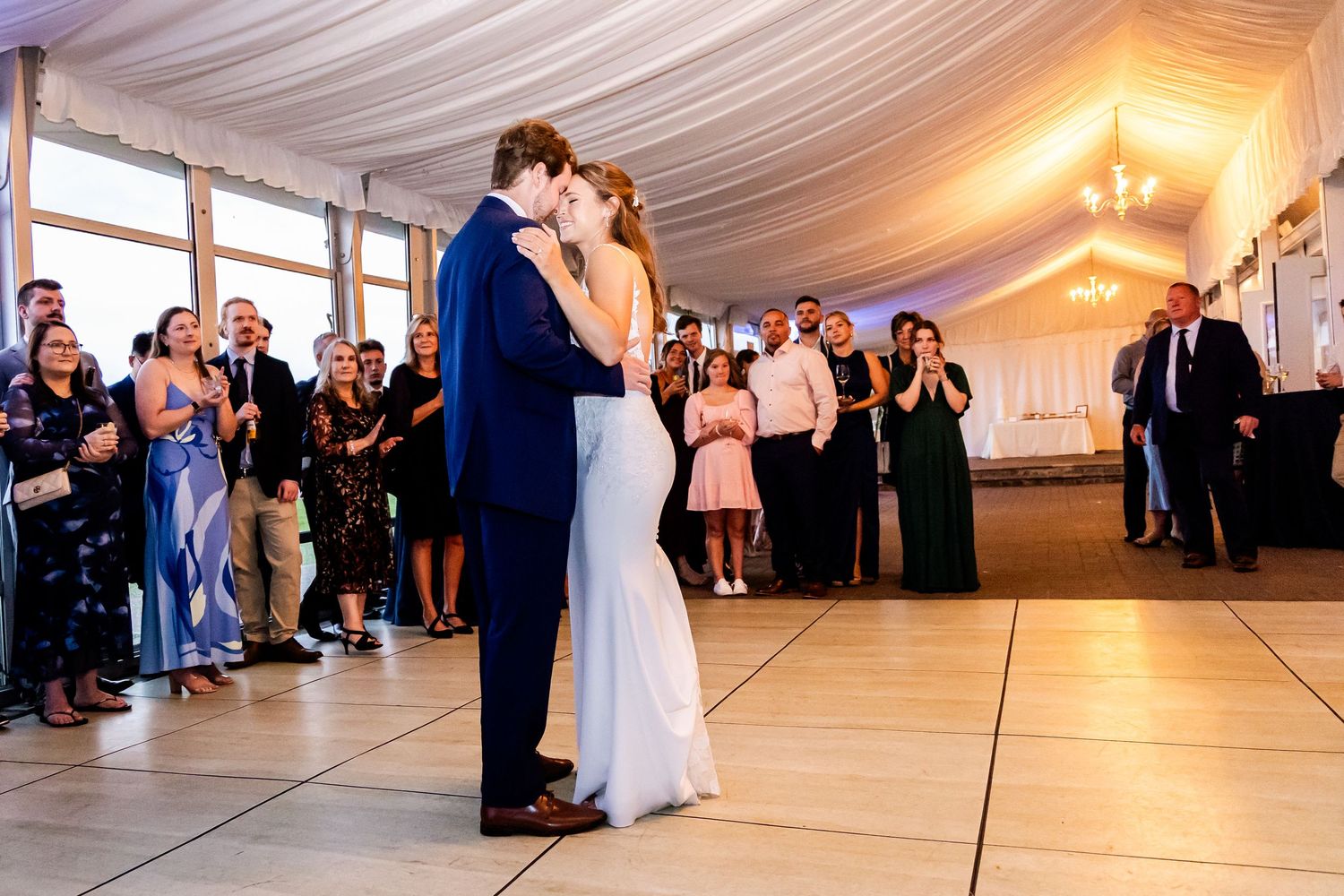 A couple shares their first dance in an elegant white-draped reception tent.