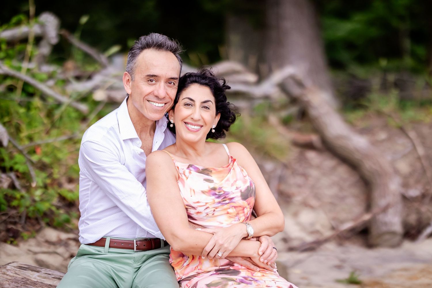 A couple sits together on rocky terrain near a stream during a romantic outdoor photoshoot.
