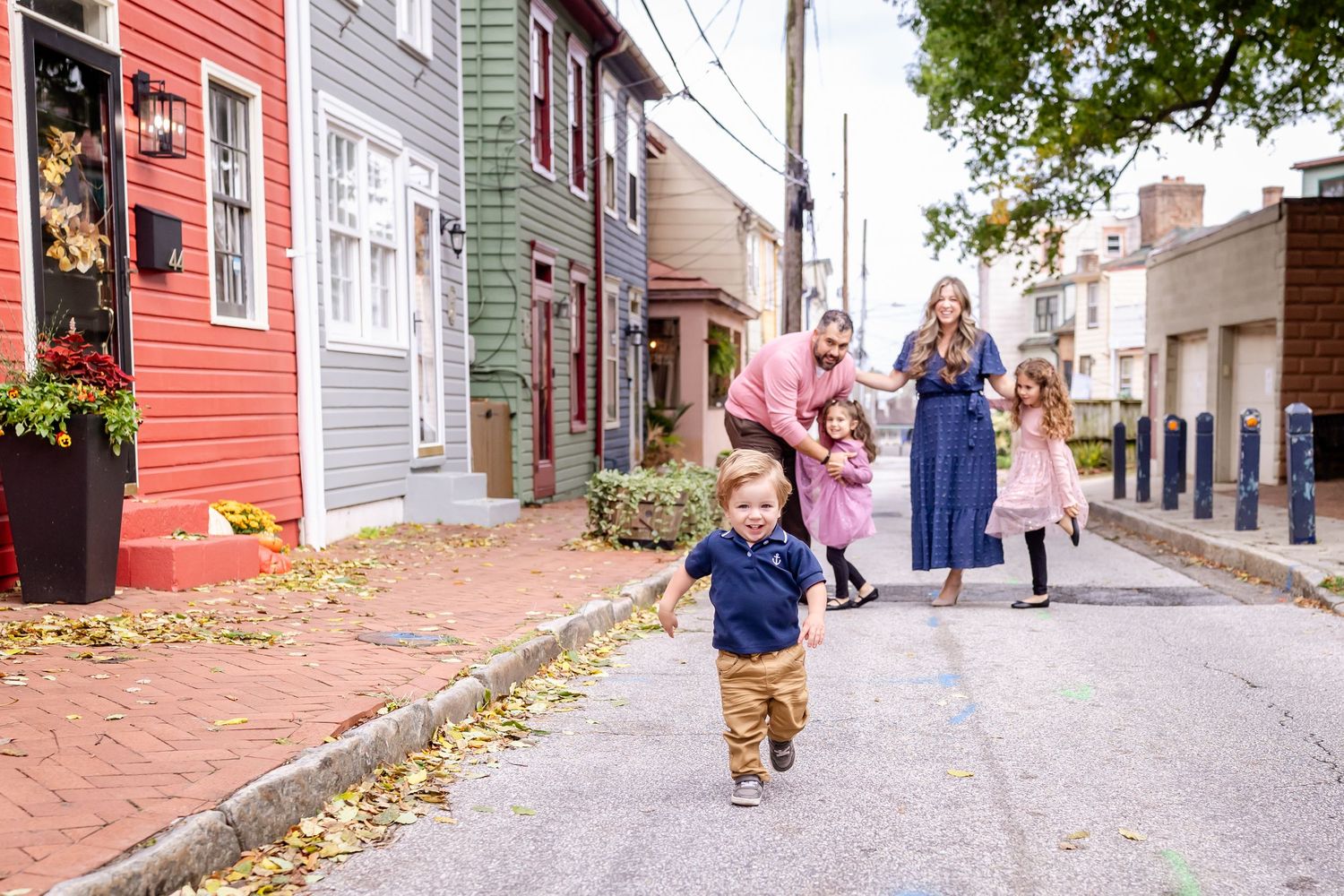 People walk along a historic cobblestone street lined with colorful buildings in an old town neighborhood.