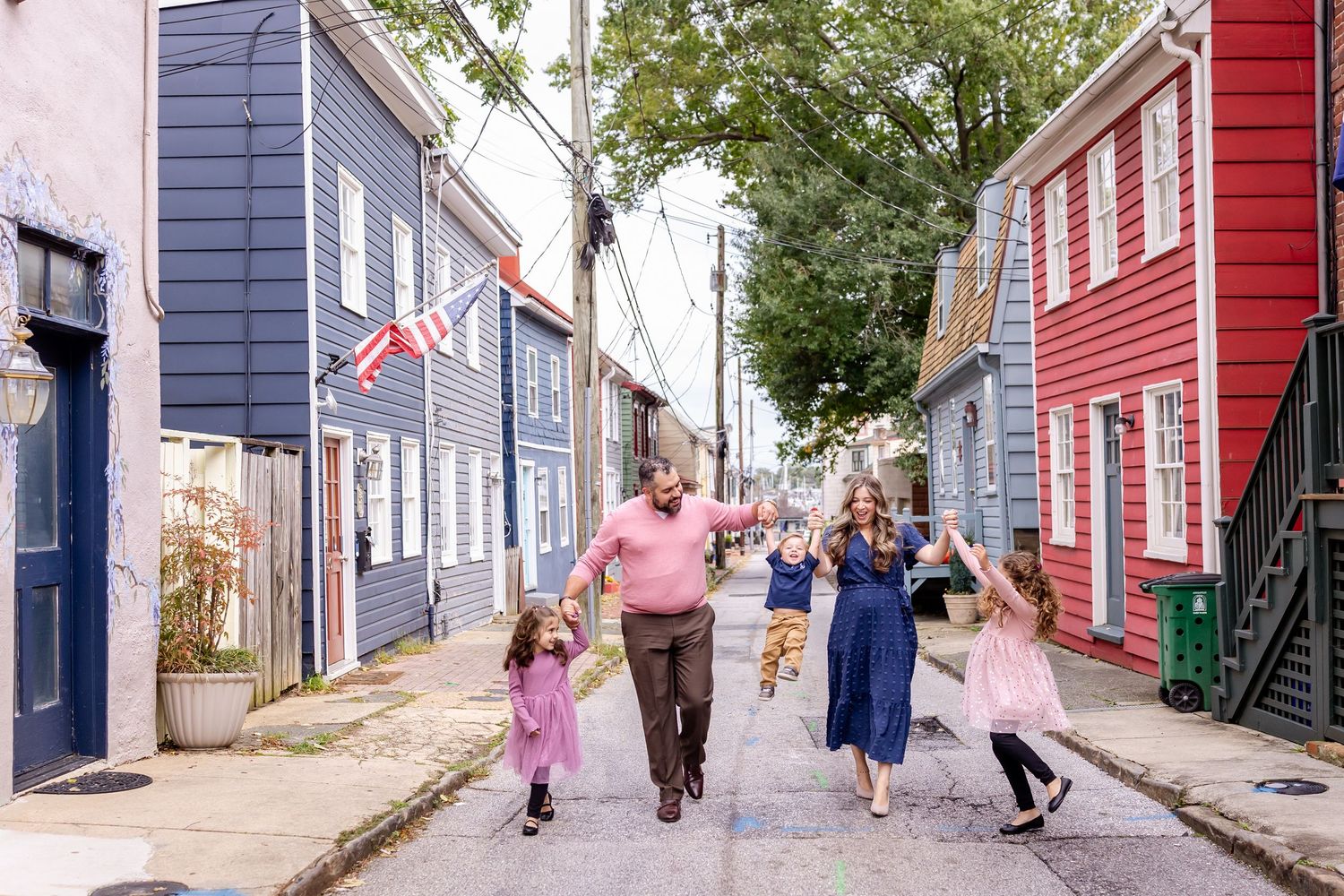 People walk along colorful row houses on a narrow cobblestone street in Baltimore's historic district.