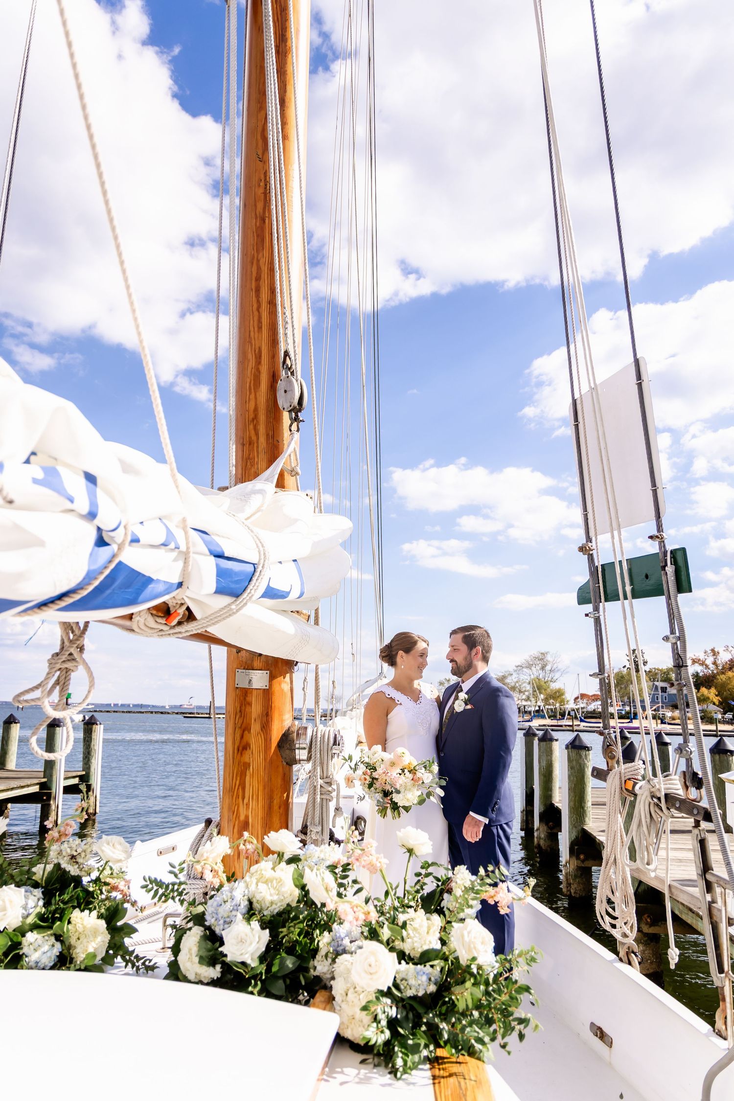 Bride and groom share a romantic moment on a decorated sailboat at a sunny harbor wedding.