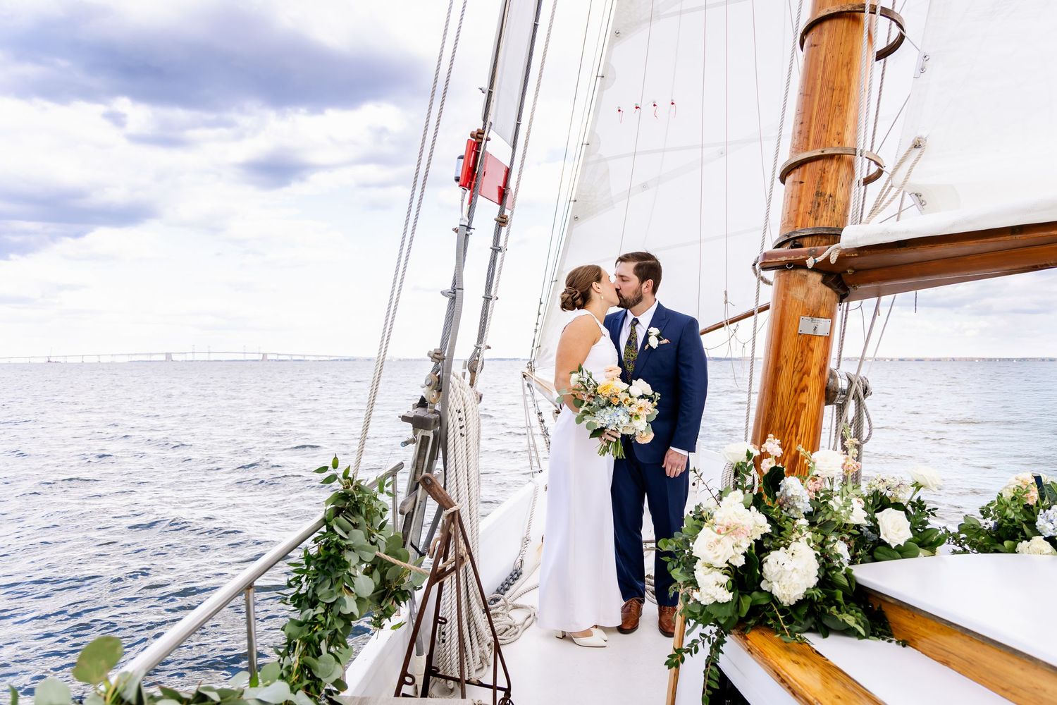 Bride and groom kissing on a decorated sailboat deck with ocean views on their wedding day.