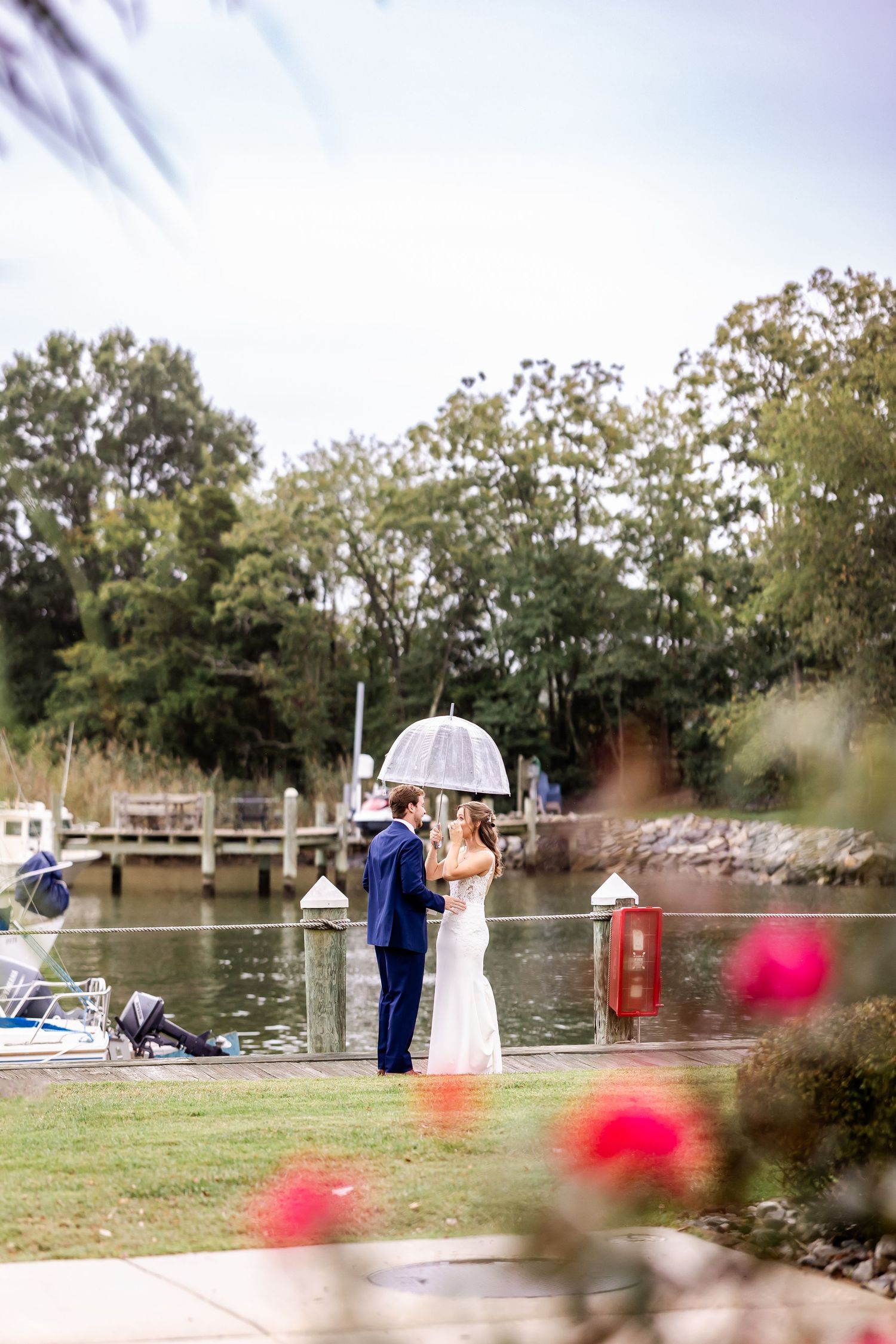 Outdoor waterfront wedding ceremony setup with red flowers in the foreground and boats docked in the background.