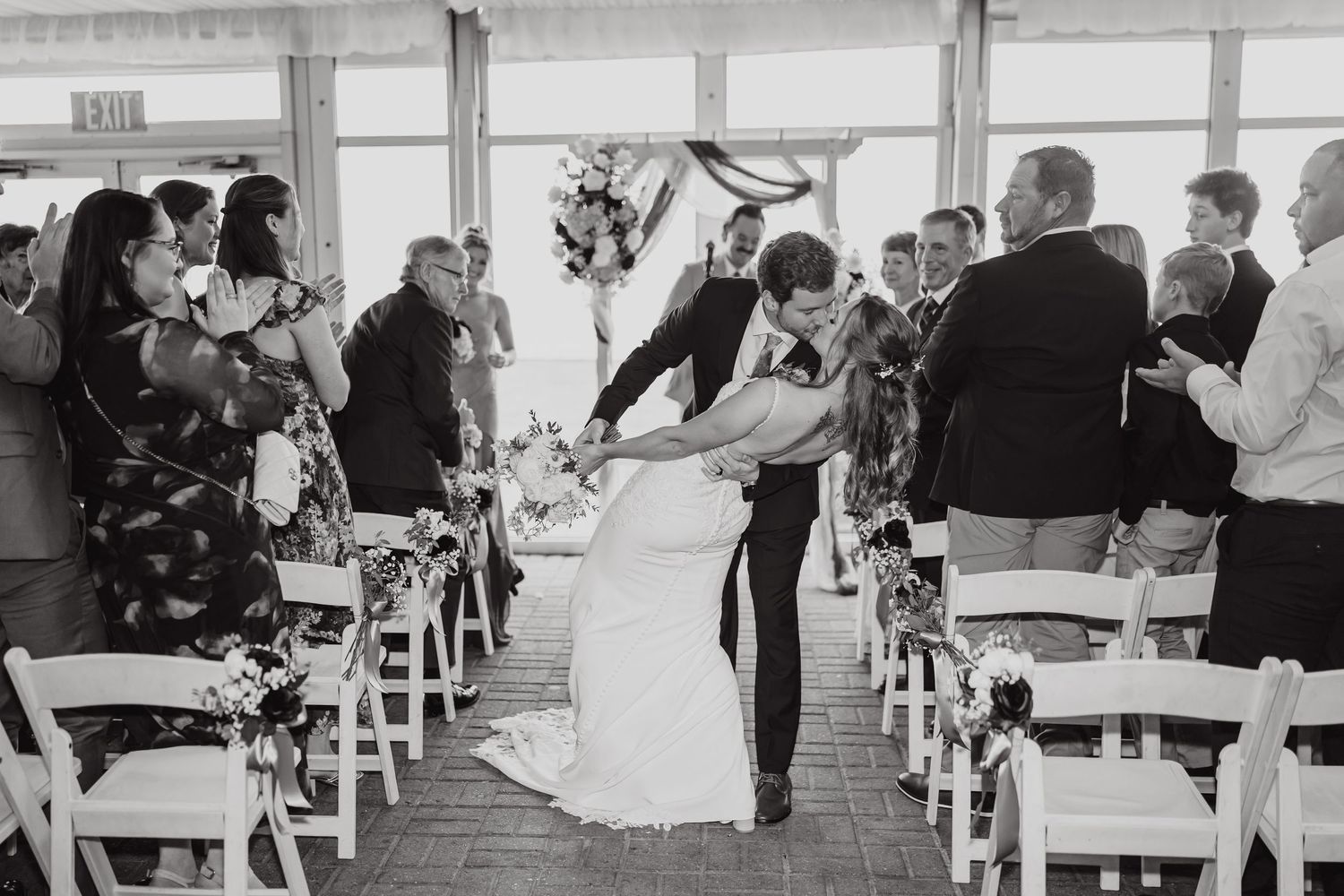 Black and white photo of wedding reception with guests seated at decorated tables.