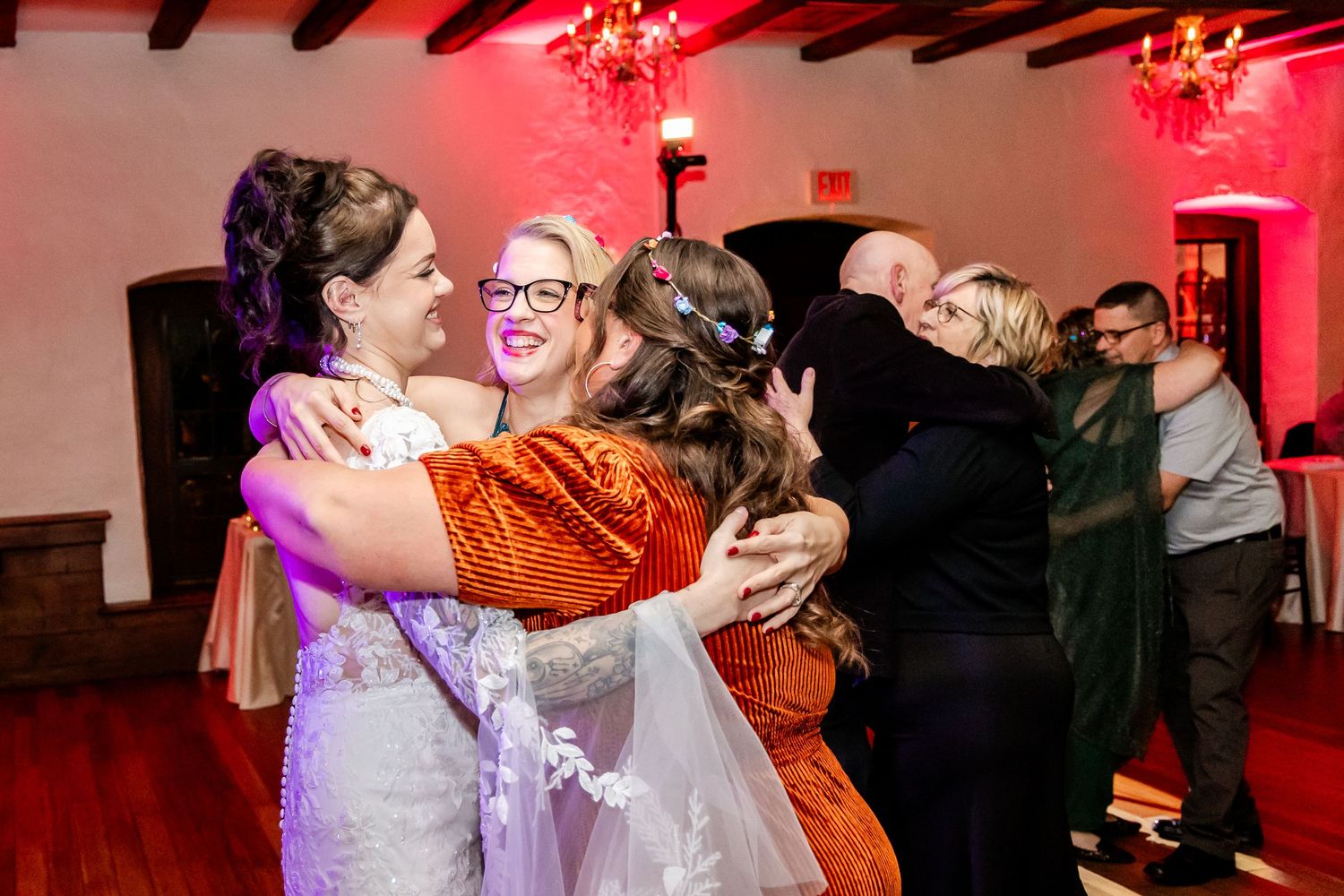 Wedding reception dance party with dramatic red lighting and exposed wooden beams overhead.
