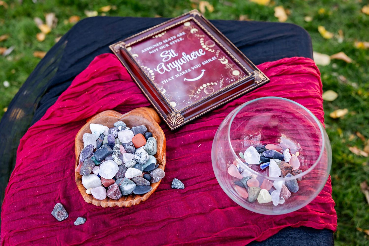 Decorative stones and wedding signs arranged on red velvet fabric outdoors.