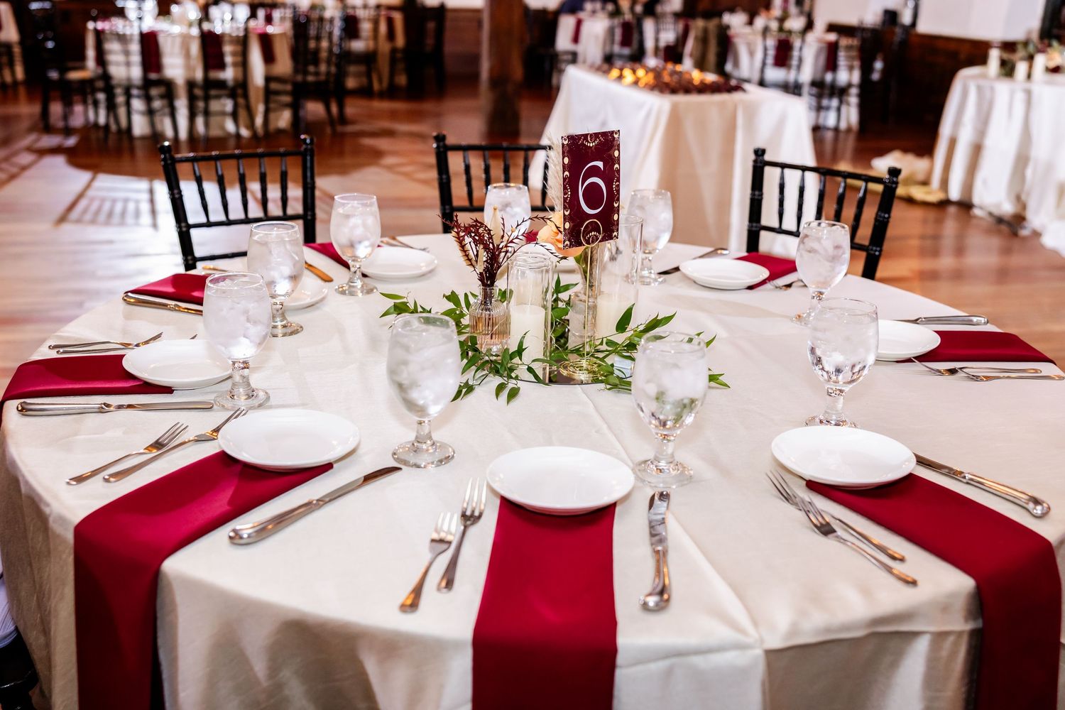 Elegant wedding reception tables set with white linens and burgundy accents.