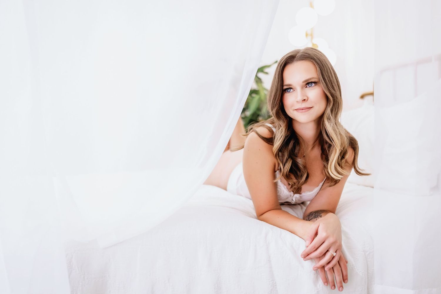 A woman in a white dress poses against a light background with soft, wavy hair and natural makeup.