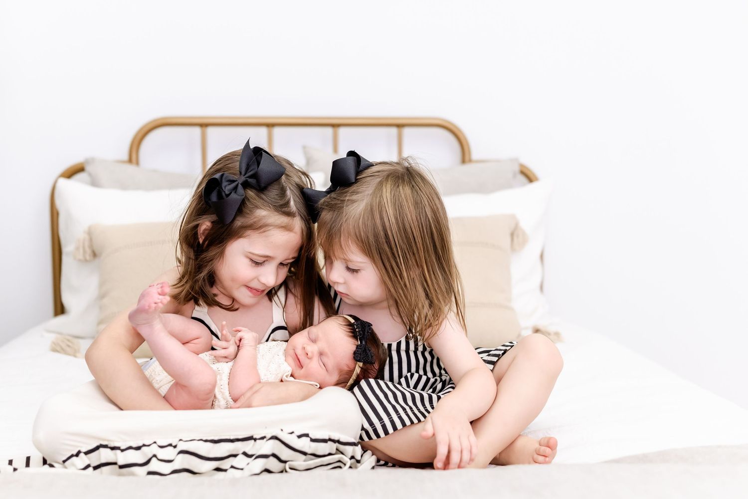 Two young children in black and white outfits share a tender moment while sitting together on a white bed.