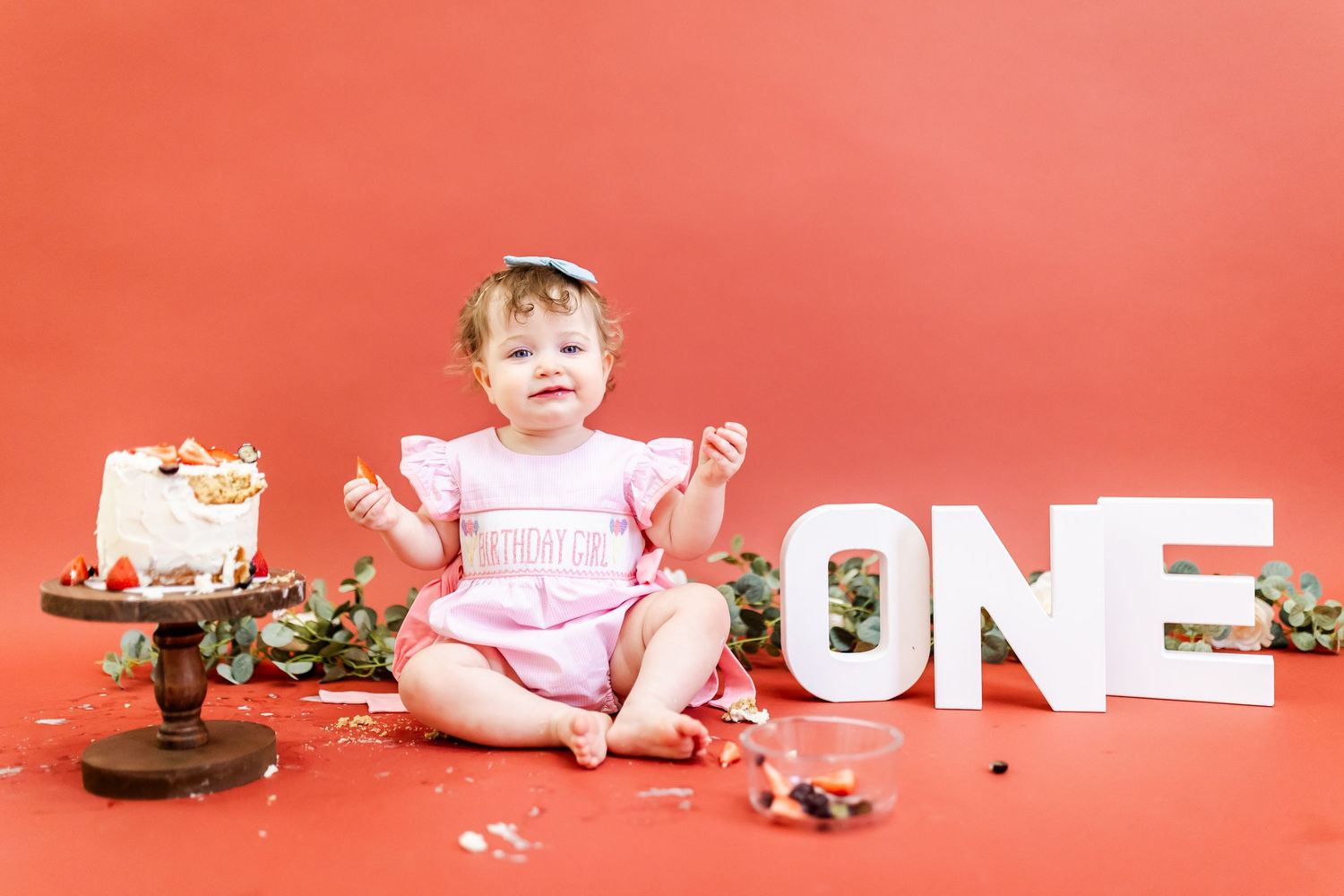 A cake smash photo session shows a progression of a baby in pink dress enjoying and destroying a birthday cake.