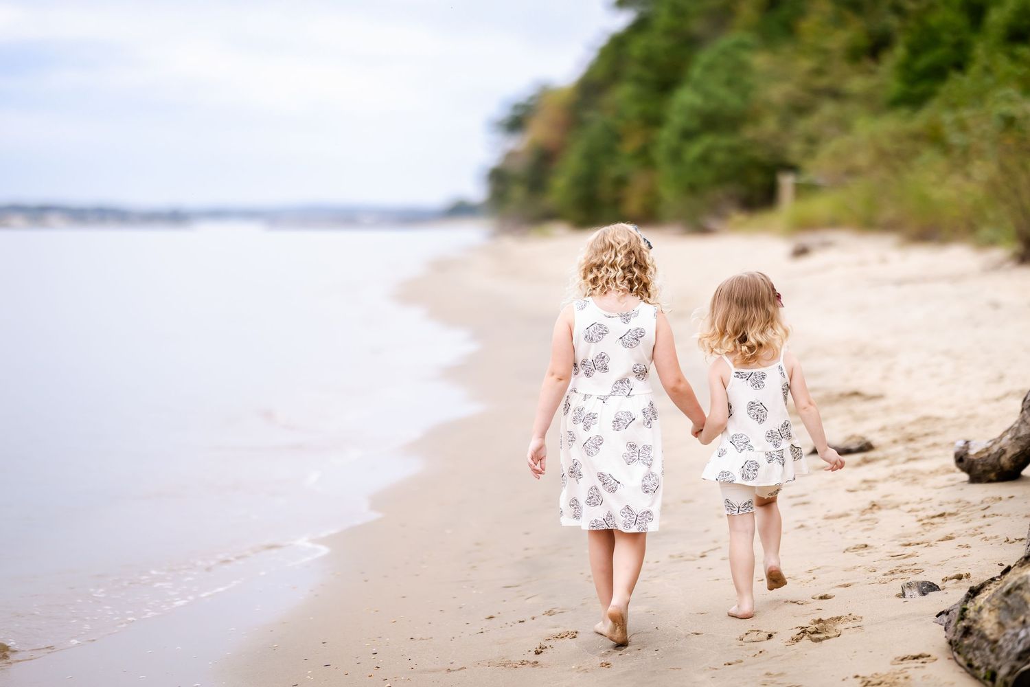Two people in white outfits walking along a serene beach shoreline on a sunny summer day.