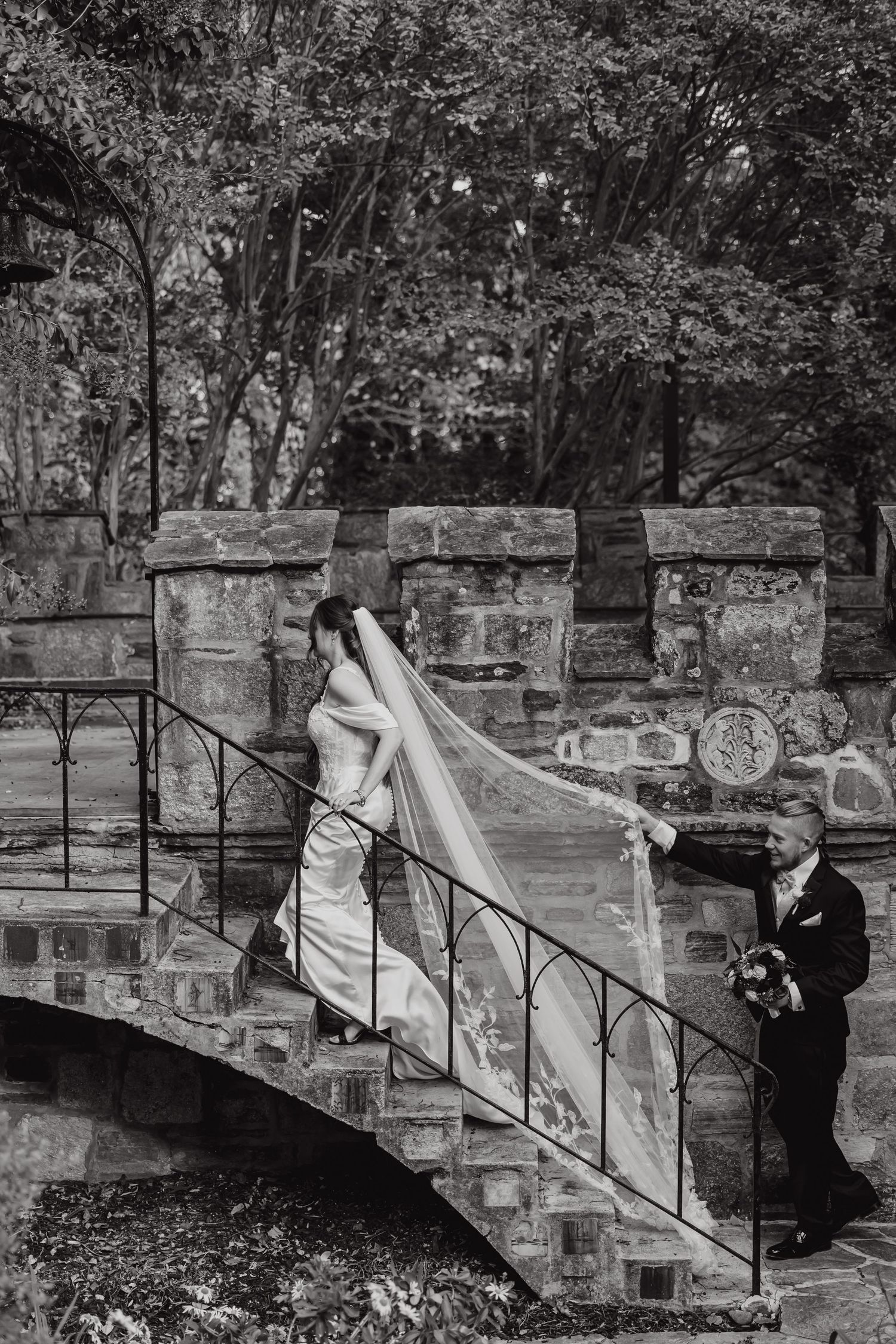 A romantic black and white photo series showing a couple on stone steps with an iron railing in a garden setting.