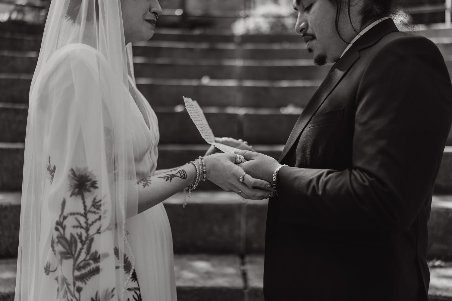 A black and white photo showing a couple exchanging rings during an outdoor wedding ceremony.