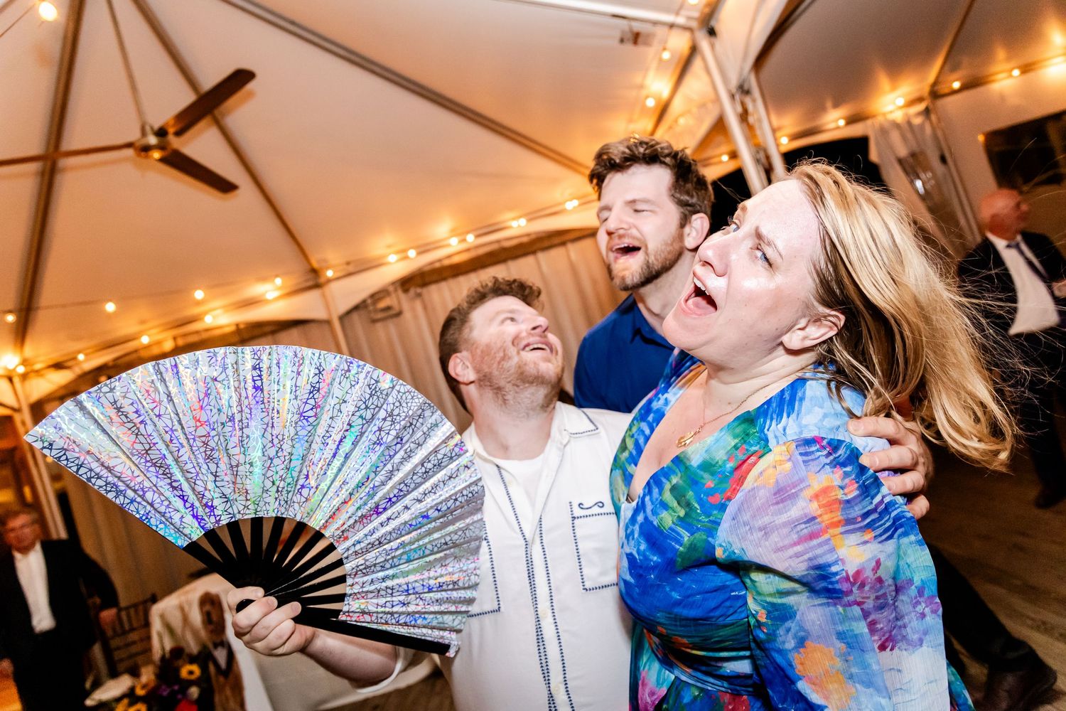 People dance and celebrate at a lively party with string lights and colorful decorations overhead.