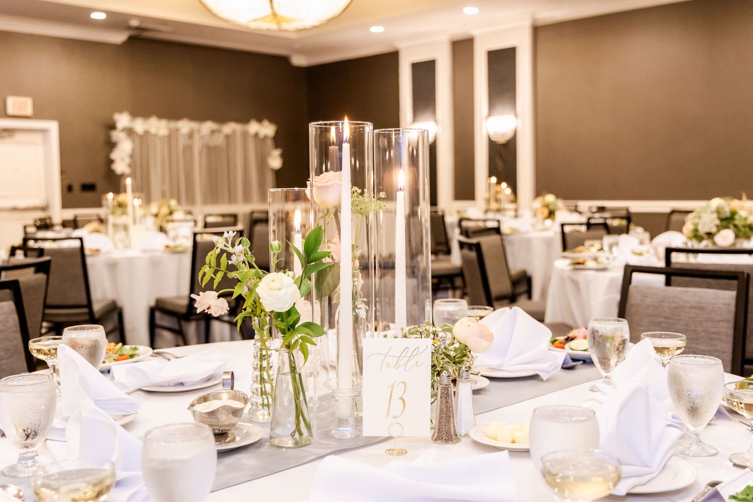 Elegant wedding reception setup with white linens, tall centerpieces and modern lighting in neutral tones.