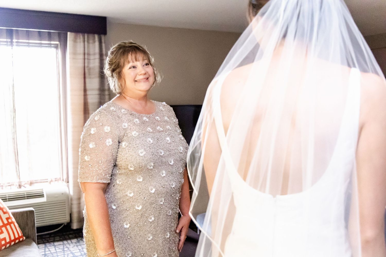 A bride in a sparkling beaded gown stands by a window with her flowing veil.