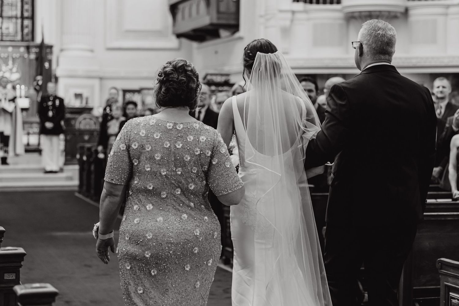 Wedding guests watching ceremony in classic white-columned interior space.