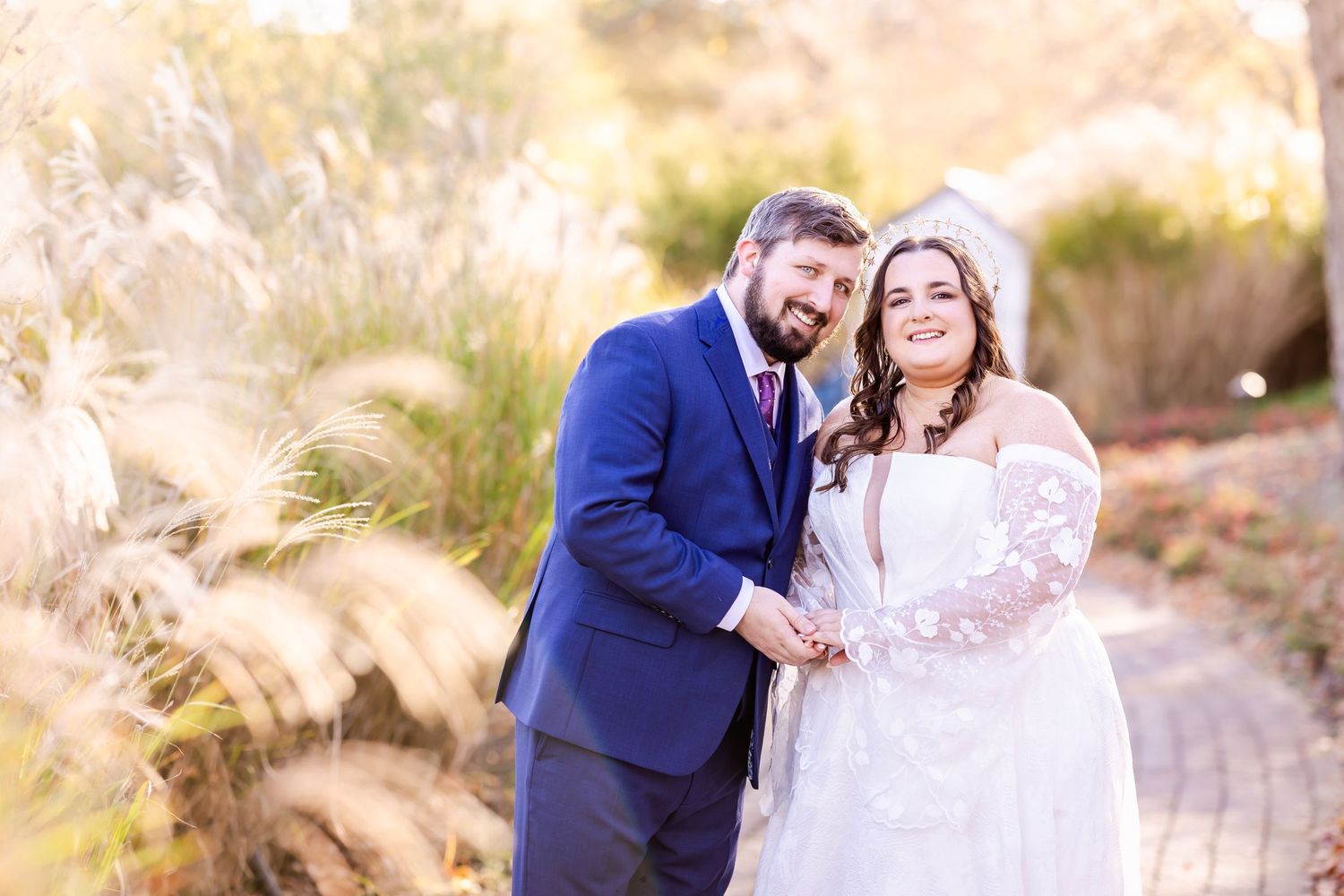 A joyful wedding couple poses together in a garden setting with golden sunlight.