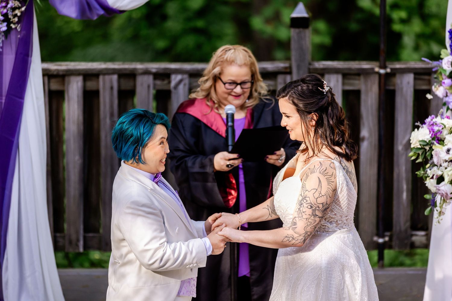A touching wedding ceremony moment under an arch decorated with purple and white fabric.