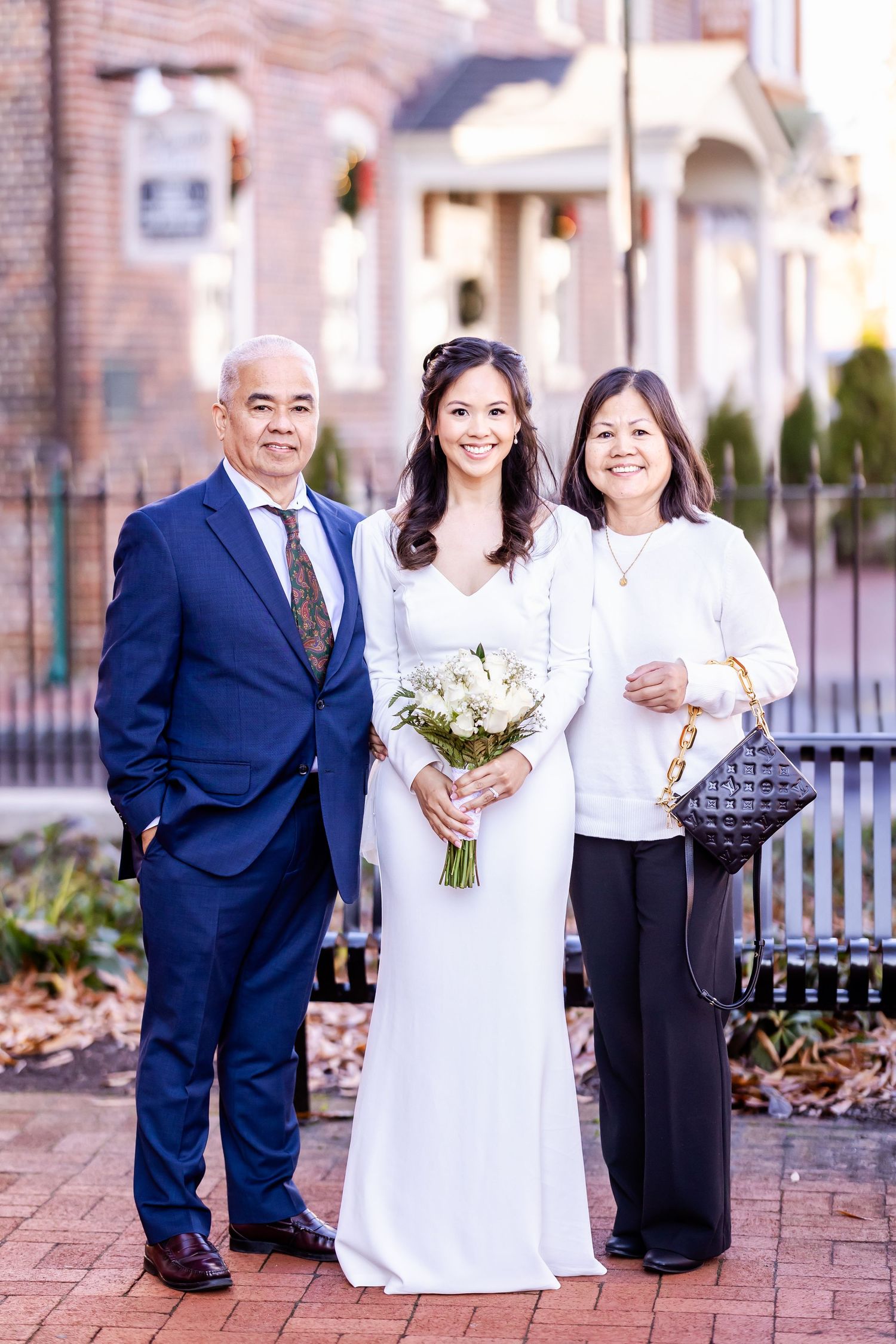 A beautiful bride in a white gown poses with family outside a brick building.