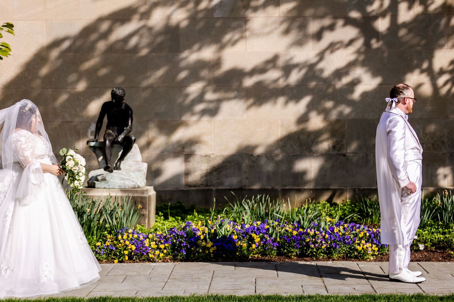 Wedding ceremony in garden with blooming flowers and dramatic tree shadows on stone wall.