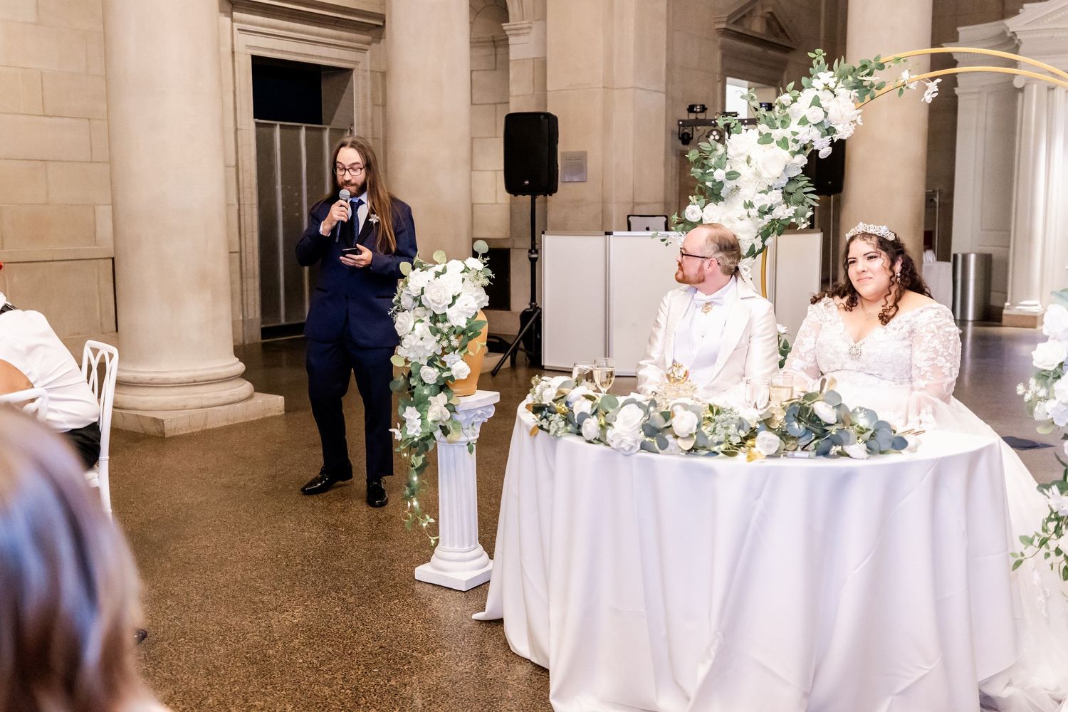 Wedding reception setup in elegant venue with white table decor and floral arrangements.