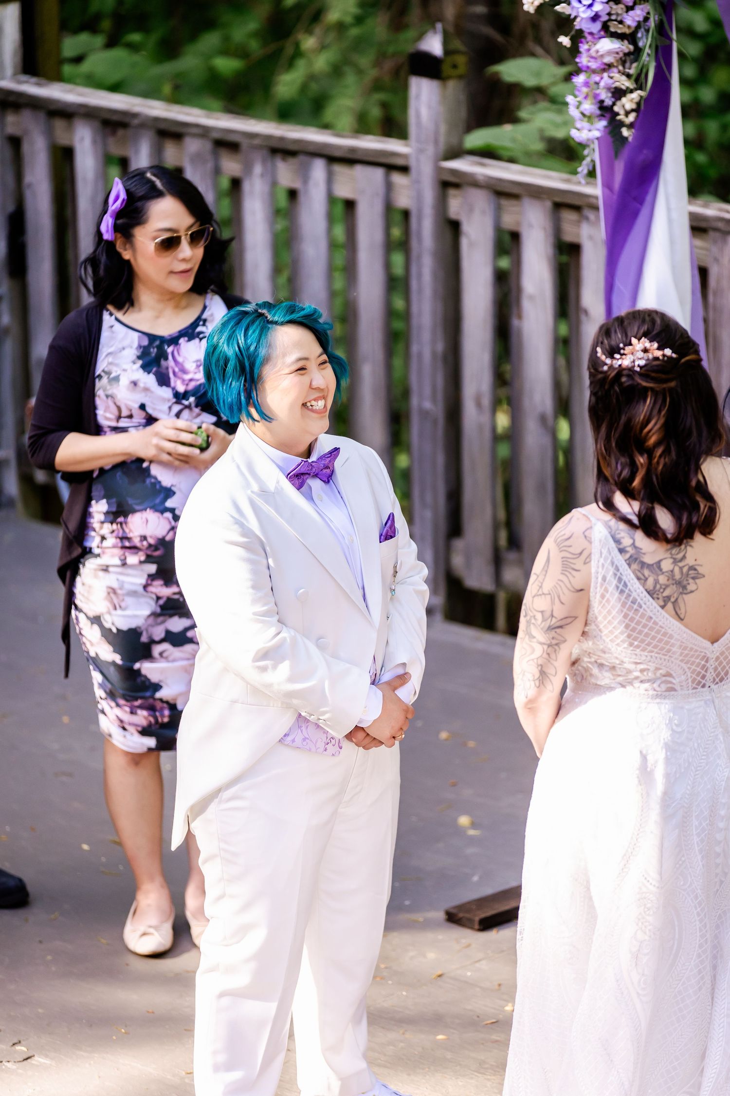 Wedding participants share a joyful moment on a wooden deck during an outdoor ceremony.