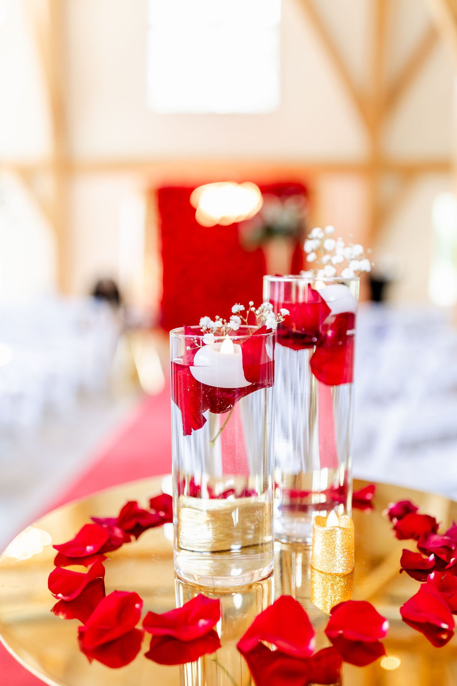 Decorative glass vases with floating red rose petals on gold tray for wedding centerpiece.