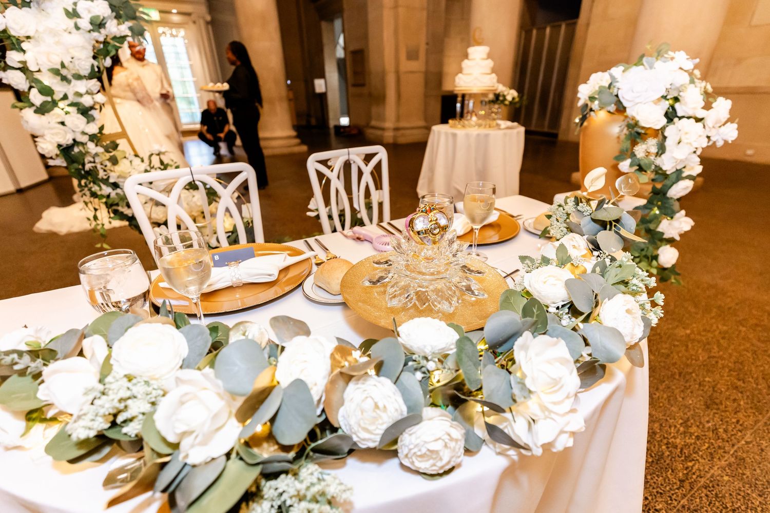 Elegant sweetheart table decorated with white roses and eucalyptus at a wedding reception.