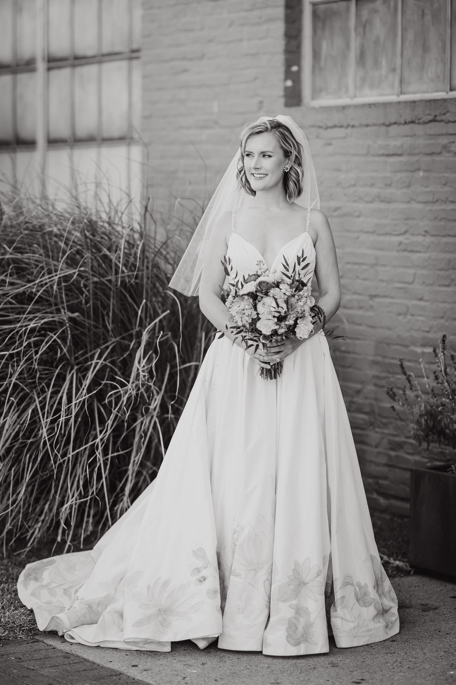 A bride in a classic white wedding gown holds a bouquet while posing against a brick wall.