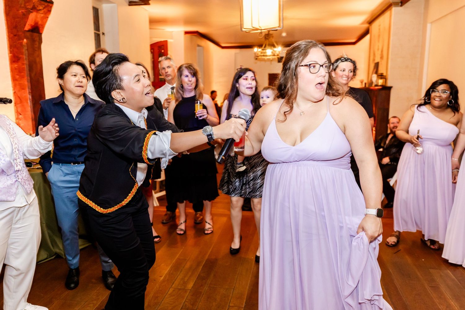 Wedding guests dancing and celebrating on a hardwood floor under pendant lighting.