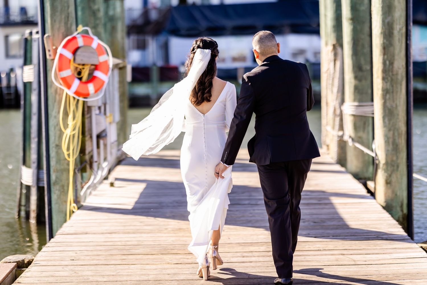 A couple walks hand in hand down a wooden pier with a life preserver visible.