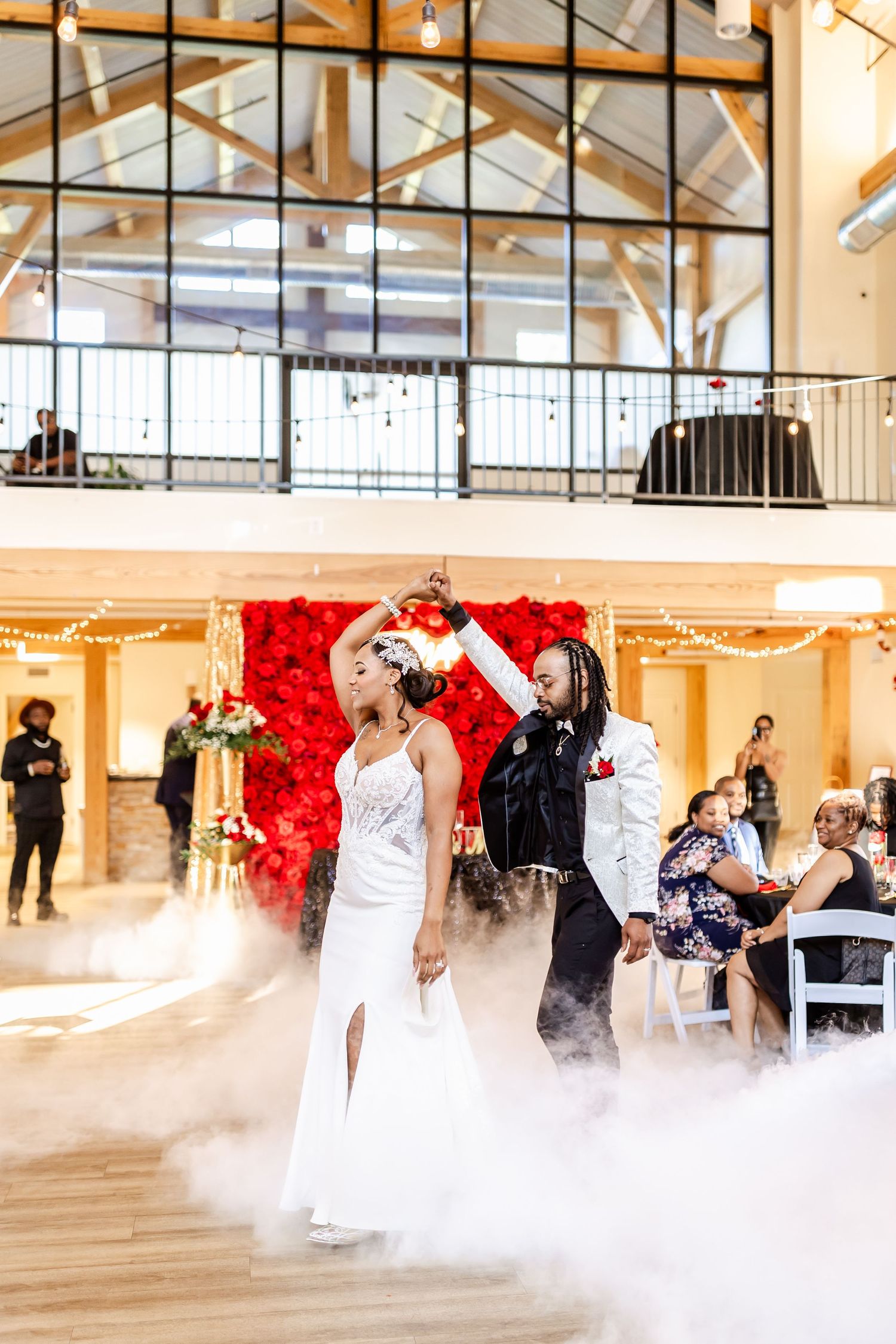 Wedding celebration with dramatic fog effects on dance floor featuring a red rose wall and high vaulted ceiling.