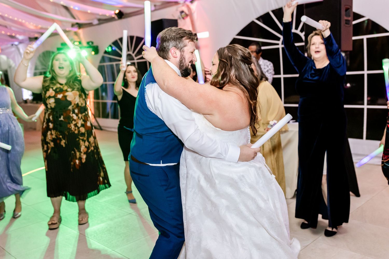 Energetic dancing at wedding reception with colorful lighting and decorated tent ceiling.