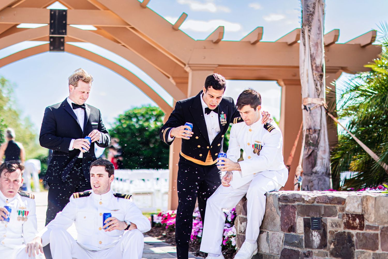 Groomsmen relaxing and enjoying drinks on an outdoor patio with wooden pergola and stone pillars.