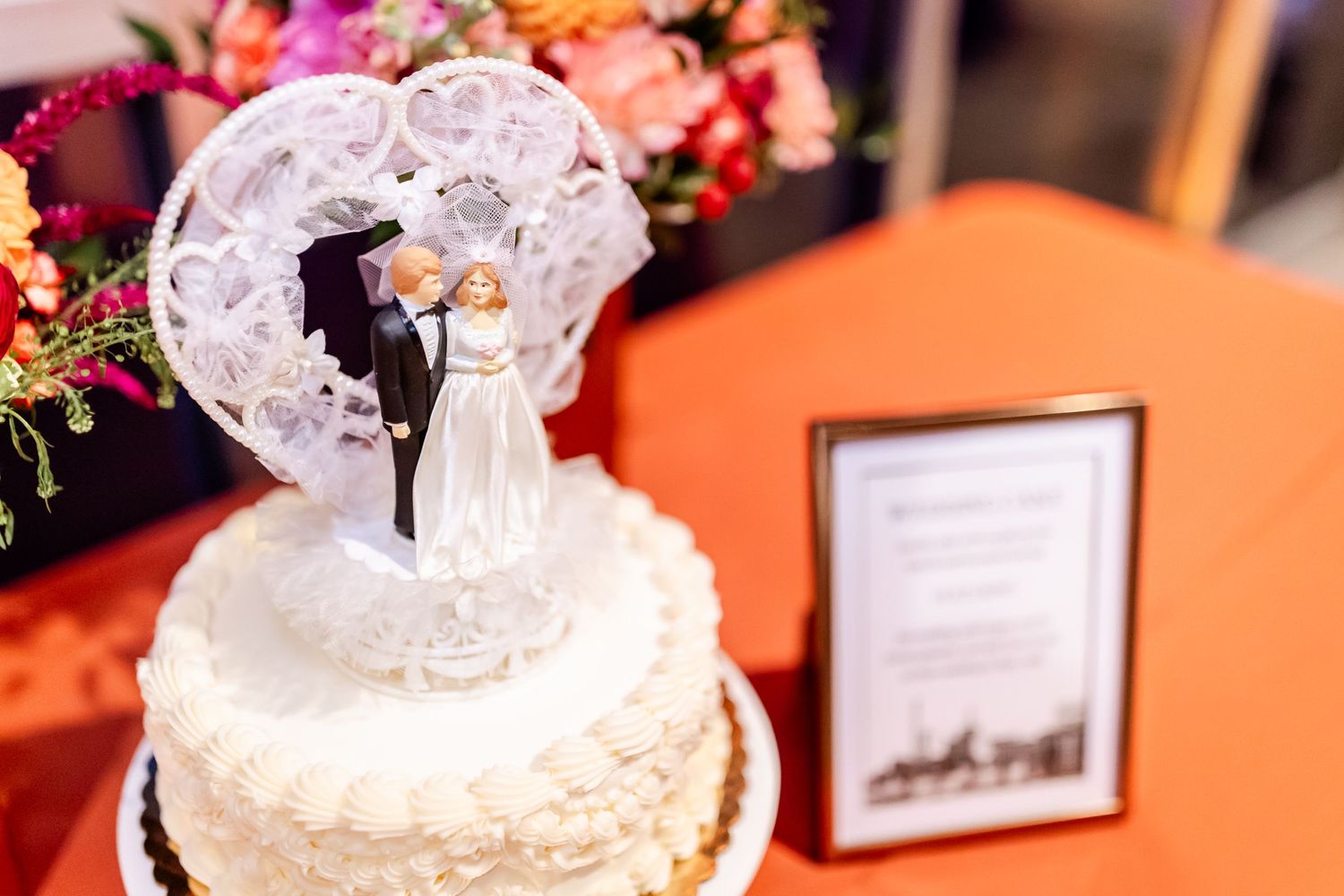 Elegant white wedding cake topped with a sparkly silhouette cake topper surrounded by floral decorations.
