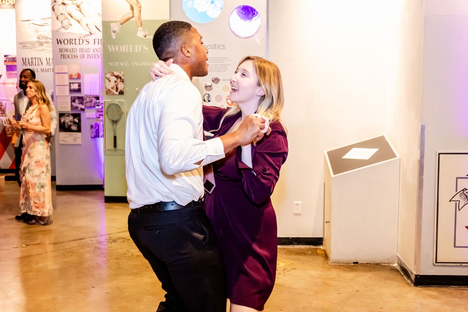Couple dancing together at indoor event venue with purple lighting.