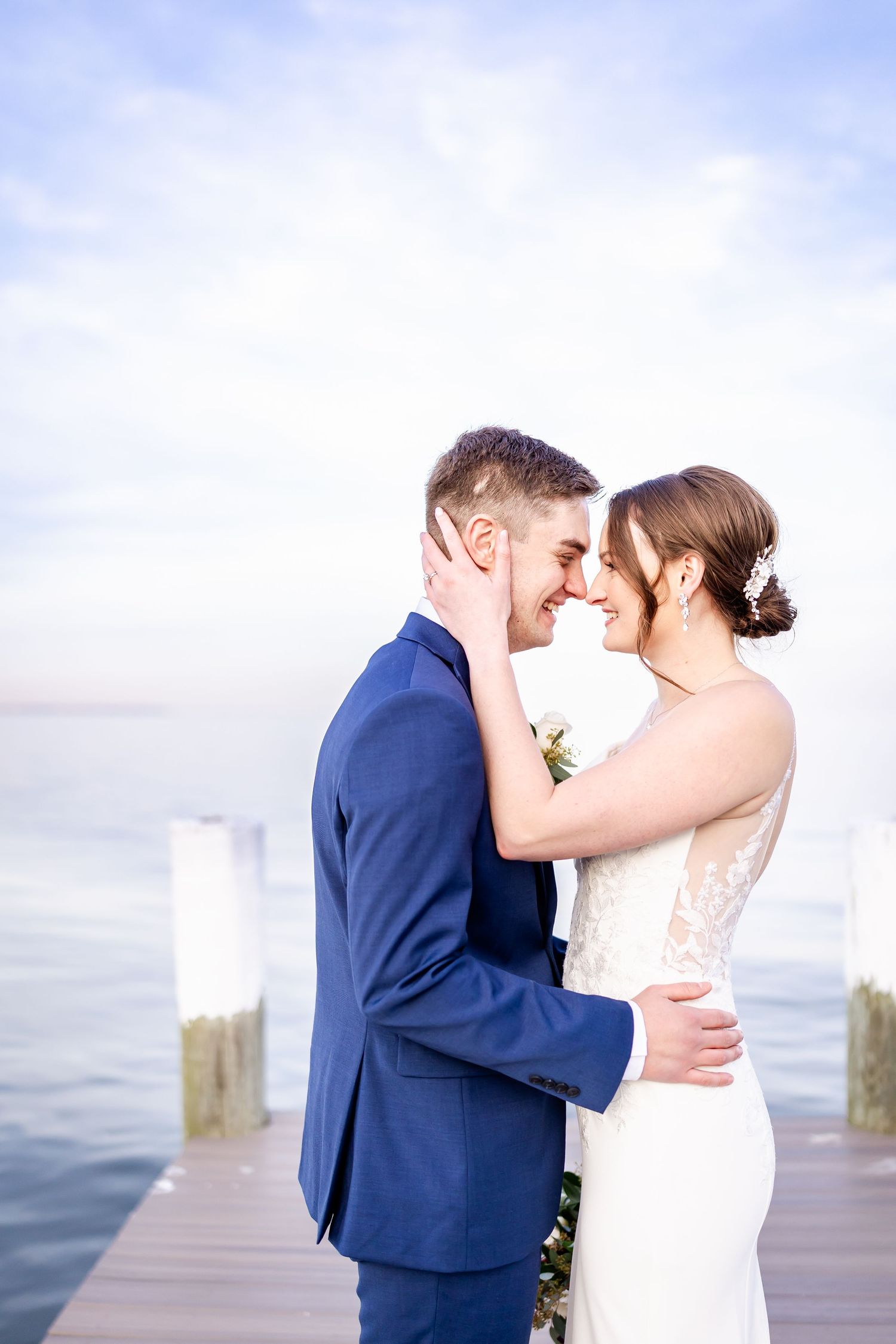 Romantic couple embraces on a wooden dock overlooking calm waters at sunset.
