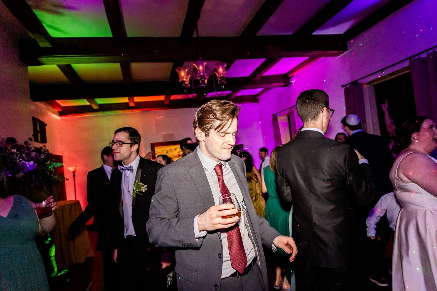Guests dancing and mingling at a wedding reception with colorful purple lighting.