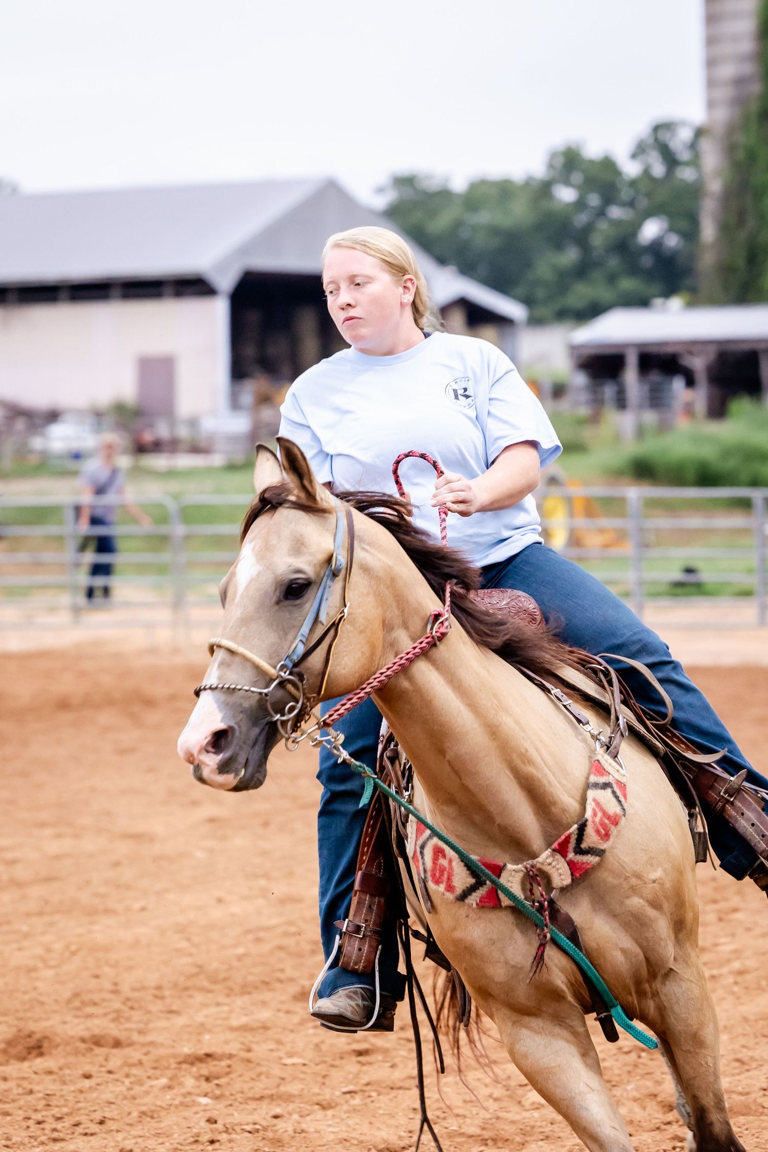 Rider racing on palomino horse through dirt arena during competition event.