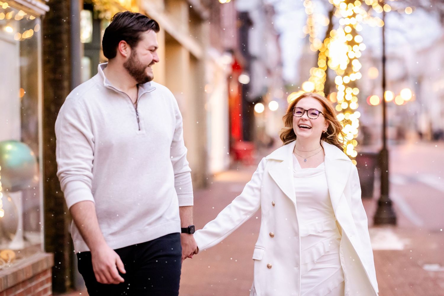 Couple walking together on a city street decorated with holiday lights and bokeh in the background.