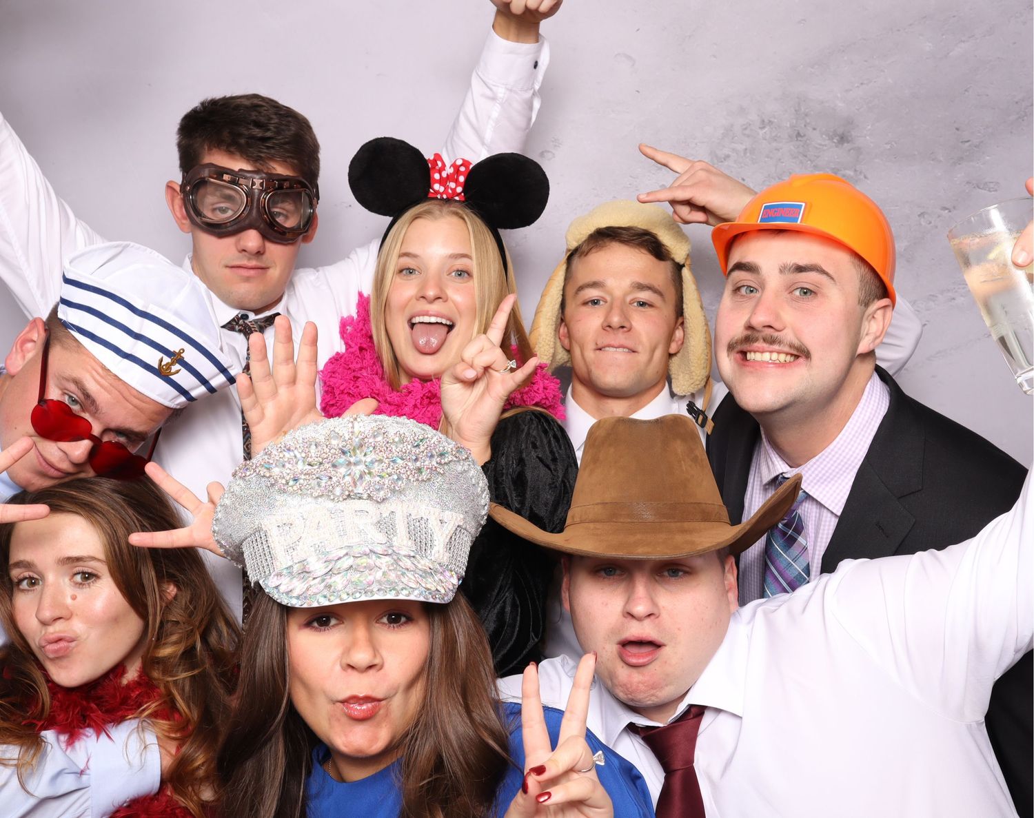 A group poses playfully at a photo booth wearing various costume accessories and party hats.