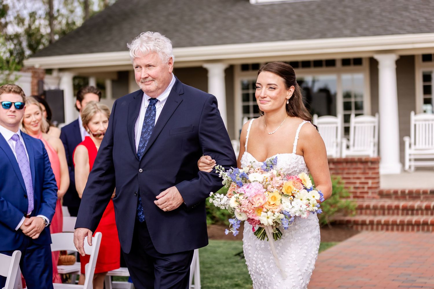 Wedding party and guests gathered outside a traditional brick home with white columns.