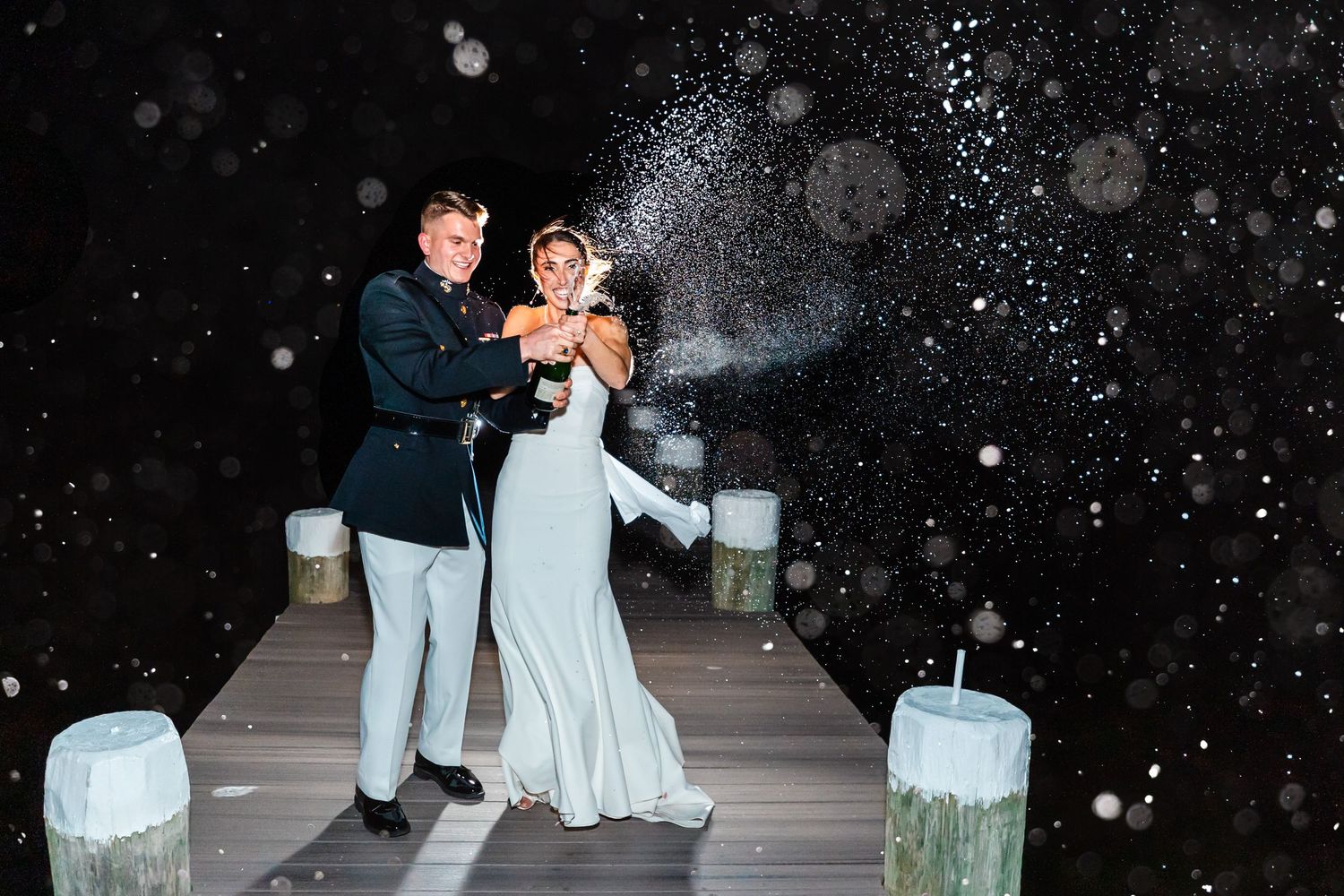 A couple celebrates on a snow-covered dock at night with glowing lights and whimsical snowflakes falling around them.