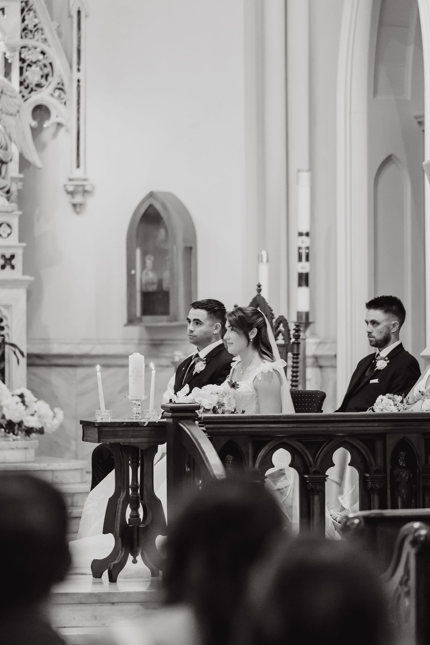 Black and white photo of wedding ceremony in traditional church with ornate wooden details.