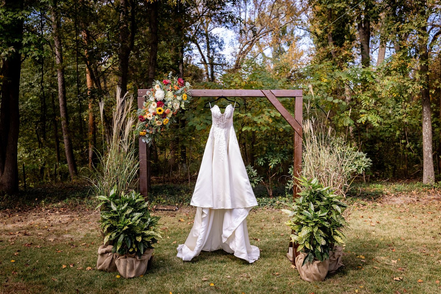 Outdoor wedding setup with wooden arch and floral arrangements in a wooded garden setting.